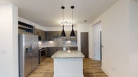 This single-floor residence showcases a contemporary design with consistent, light-toned wood-look flooring and crisp white walls throughout, creating a clean and cohesive aesthetic. The kitchen serves as a focal point of the home, featuring dark taupe cabinetry with sleek hardware, granite countertops, a tiled backsplash, and a full suite of stainless steel appliances including a French door refrigerator, range, built-in microwave, and dishwasher. A central island with a granite top provides additional prep space and casual seating, while two bold pendant lights overhead add a modern design statement. An integrated wine rack adds a distinctive touch to the cabinetry.

The living area is generously proportioned with multiple windows that invite natural light and access to an exterior door. A ceiling fan provides comfort throughout the space. The bedrooms are well-sized, each benefiting from natural light through double windows and ceiling fans, with neutral walls ready for personalization.

The bathrooms are finished to a high standard. The primary bath features a double-sink vanity with granite countertops, dark cabinetry, and a large framed mirror. A secondary full bathroom includes a granite-topped vanity and a tub-shower combination with large-format marble-style tile surround, completing the refined and functional design of this modern residence.