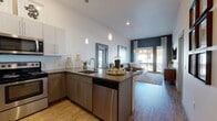 Located at 1420 Oak St in Lakewood, Colorado, this thoughtfully designed single-floor residence combines modern aesthetics with functional living. The open-concept layout seamlessly connects the kitchen, dining, and living areas, creating a cohesive and inviting atmosphere. The kitchen is equipped with stainless steel appliances, including a refrigerator, range, microwave, and dishwasher, and features two-tone cabinetry — crisp white upper cabinets paired with warm wood-toned lower cabinets — topped with sleek quartz-style countertops. A peninsula with bar seating provides additional dining and gathering space, while pendant lighting adds a contemporary touch. The living area is bright and airy, with tall ceilings, wood-style flooring, and large windows and a sliding glass door that invite abundant natural light and outdoor views. The bedroom is a calm retreat, highlighted by a bold dark accent wall, plush carpeting, and generous natural light from a sizeable window. An en-suite bathroom features a wood-toned vanity with stone countertops, tile-surround soaking tub and shower combination, and warm wood-look flooring. The overall design palette of neutral tones, modern fixtures, and carefully chosen finishes creates a cohesive, contemporary ambiance throughout the residence.