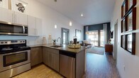 Located at 1420 Oak St in Lakewood, Colorado, this thoughtfully designed single-floor residence combines modern aesthetics with functional living. The open-concept layout seamlessly connects the kitchen, dining, and living areas, creating a cohesive and inviting atmosphere. The kitchen is equipped with stainless steel appliances, including a refrigerator, range, microwave, and dishwasher, and features two-tone cabinetry — crisp white upper cabinets paired with warm wood-toned lower cabinets — topped with sleek quartz-style countertops. A peninsula with bar seating provides additional dining and gathering space, while pendant lighting adds a contemporary touch. The living area is bright and airy, with tall ceilings, wood-style flooring, and large windows and a sliding glass door that invite abundant natural light and outdoor views. The bedroom is a calm retreat, highlighted by a bold dark accent wall, plush carpeting, and generous natural light from a sizeable window. An en-suite bathroom features a wood-toned vanity with stone countertops, tile-surround soaking tub and shower combination, and warm wood-look flooring. The overall design palette of neutral tones, modern fixtures, and carefully chosen finishes creates a cohesive, contemporary ambiance throughout the residence.