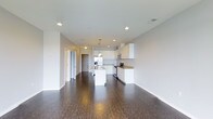This two-bedroom, two-bathroom unit offers a well-designed, single-level floor plan with an open-concept layout that connects the kitchen and living areas seamlessly. The kitchen is a standout feature, showcasing crisp white cabinetry that extends to the upper walls, granite-style countertops, and stainless steel appliances including a range, microwave, and refrigerator. A central kitchen island with a sink provides additional workspace and acts as a natural dividing point between the kitchen and the expansive living area. Pendant lighting hangs above the island, complementing the recessed ceiling lights that illuminate the space evenly. Rich, dark hardwood-style flooring runs throughout the main living area, creating a bold contrast against the white cabinetry and light-toned walls. The open layout lends a sense of spaciousness, while the neutral color palette provides a versatile backdrop for various design preferences. A hallway visible from the main living area leads to the bedrooms and bathrooms, offering a practical and well-organized flow throughout the unit.
