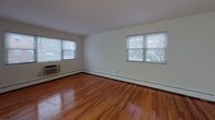 This single-floor unit offers a clean, functional layout with warm hardwood flooring that flows consistently throughout the living areas and bedroom. The open living room is generously sized, featuring two large windows that invite abundant natural light and views of the surrounding neighborhood. A wall-mounted air conditioning unit and baseboard heating ensure year-round comfort.

The kitchen is efficiently designed with rich, dark espresso-toned cabinetry, granite-style countertops, a black gas range, and a stainless steel sink — providing everything needed for everyday cooking. The layout maximizes available counter and storage space.

The bedroom continues the hardwood flooring theme and includes a built-in closet with shelving, offering practical storage solutions. A separate entry door with secure hardware connects the unit to the building's common areas.

The bathroom is finished in classic white subway tile surrounding the tub-shower combination, complemented by chrome fixtures, a white vanity with sink, and a mirrored medicine cabinet. A frosted window provides natural light while maintaining privacy.

Throughout the unit, white walls create a bright, neutral backdrop that enhances the sense of space. The overall ambiance is clean, practical, and move-in ready, with timeless finishes that suit a variety of furnishing styles.