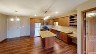 This single-floor residence offers a thoughtfully designed layout with a cohesive blend of warm wood tones, granite surfaces, and neutral wall colors throughout. The kitchen serves as a central highlight, featuring rich medium-toned cabinetry, granite countertops, stainless steel appliances including a refrigerator, range, and dishwasher, and a central island topped with matching granite beneath stylish pendant lighting. Open wire shelving adds a practical storage accent, while hardwood flooring grounds the space with warmth. A stone-surround fireplace anchors the living area, adding a classic focal point. The layout includes carpeted bedrooms, each offering baseboard heating and windows with scenic views of the surrounding landscape. The bathroom is well-equipped with granite vanity countertops, rich wood cabinetry, a tub-shower combination, and a conveniently integrated stacked washer and dryer unit. Elegant arched doorways add architectural character to the interior hallways. A spacious walk-in closet with wire shelving provides ample storage and connects directly to a bathroom. An outdoor deck extends the living space and offers additional outdoor enjoyment.