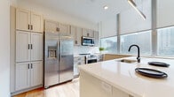Located at 200–254 Frankfort Ave in Cleveland, Ohio, this single-floor unit offers a well-designed, contemporary living space with a cohesive aesthetic carried throughout. The kitchen is a standout feature, outfitted with stainless steel appliances including a full-size refrigerator, range, microwave, and dishwasher. Light gray shaker-style cabinetry pairs with white quartz countertops and a classic subway tile backsplash, while floor-to-ceiling windows flood the space with natural light and frame views of the surrounding Cleveland cityscape. Light hardwood flooring extends through the kitchen and into the hallway and living areas, creating a seamless flow. The living room is generously proportioned, anchored by a white fireplace and expansive floor-to-ceiling windows that continue the urban view. A wide, light-filled hallway connects the main living areas to the private spaces, including a well-appointed bedroom with plush carpeting and a roller shade window treatment. The bathroom features large-format tile flooring and a glass-enclosed walk-in shower with white subway tile surround and matte black hardware accents. Throughout the unit, clean lines, neutral tones, and abundant natural light combine to create a bright, modern, and inviting atmosphere well-suited to urban living.