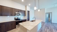 This well-designed single-floor residence offers a thoughtfully laid-out open-concept floor plan that seamlessly connects the kitchen, dining, and living areas. The kitchen is a standout feature, showcasing rich dark-wood cabinetry that extends to the ceiling, a classic white subway tile backsplash, and a full suite of stainless steel appliances including a refrigerator, electric range, and over-the-range microwave. A generous kitchen island topped with light granite countertops provides an integrated sink and additional prep space, illuminated by stylish pendant lighting overhead. The open living area is finished with durable wood-look plank flooring and includes a ceiling fan, with access to a patio or balcony via vertical blinds. Bedrooms feature plush carpeting, tray ceilings, and windows that invite natural light. The primary bathroom is equipped with a glass-enclosed shower, dark wood vanity, granite countertop, and wood-look tile flooring, while the secondary bathroom offers a full tub-shower combination with tiled surround, matching vanity finishes, and chrome fixtures. Throughout the residence, a neutral color palette and clean-lined design create a contemporary and inviting atmosphere.