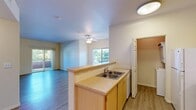 Located at 1975 Maxwell Ave in Woodland, CA, this one-bedroom, one-bathroom residence offers a well-organized single-floor layout designed for comfortable everyday living. The open-concept kitchen and living area form the heart of the home, where light wood cabinetry, a double-basin sink, tile countertops, and white appliances — including a gas range, microwave, and refrigerator — make up a fully equipped kitchen. A peninsula counter separates the kitchen from the combined dining and living area, which features wood-style flooring, a ceiling fan, and a sliding glass door that fills the space with natural light and leads to a private balcony with outdoor views. The bedroom is generously proportioned, finished with plush carpet flooring, and includes a mirrored sliding-door closet for ample storage. A second closet provides additional storage elsewhere in the unit. The full bathroom offers a soaking tub and shower combination with built-in shelving, set atop warm wood-tone flooring. A dedicated laundry area houses a stacked washer and dryer unit. The hallway connects all rooms efficiently, with neutral tones and clean finishes maintained throughout, creating a bright and cohesive living environment.