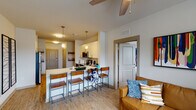 This well-appointed single-floor residential unit offers a thoughtfully designed open-concept layout that seamlessly connects the kitchen, dining, and living areas. The kitchen is a standout feature, equipped with stainless steel appliances including a range, microwave, and dishwasher, complemented by two-tone cabinetry — crisp white upper cabinets paired with rich wood-toned lower cabinets — and light quartz countertops. A peninsula with bar seating provides an ideal casual dining spot, illuminated by stylish pendant lights overhead. The living area offers a comfortable, inviting atmosphere with a ceiling fan, large windows that invite natural light, and direct sightlines into the kitchen. The unit includes multiple bedrooms, each featuring carpet flooring, windows with blinds, and ceiling fans for comfort. One bedroom showcases a sizable window with outdoor views, while another provides a quieter, more private setting with a study desk. Both full bathrooms are fitted with tub-shower combinations, brushed nickel fixtures, and vanities with granite-style countertops. Light wood-look flooring flows throughout the main living spaces, tying the open floor plan together with a clean, modern aesthetic.