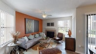 This single-floor residence offers a thoughtfully designed layout with distinct living spaces connected by wood-look flooring and a cohesive contemporary aesthetic. The living room makes an immediate impression with a bold terracotta accent wall, a tile-surround fireplace with a white mantel, and a large picture window fitted with vertical blinds that invite natural light and outdoor views. A ceiling fan with a light fixture adds functionality overhead, while the textured ceiling is consistent throughout the home.

The dining area adjoins the living space and features a sliding glass door that opens to an outdoor area, providing additional natural light and a seamless indoor-outdoor connection. A modern chandelier anchors the room above a wood dining table.

The kitchen is equipped with dark cabinetry, granite-style countertops, wood-look flooring, and black appliances including a full-size refrigerator and range.

Two bedrooms offer carpeted floors, ceiling fans, and vertical blinds. One bedroom features a charcoal accent wall, while the other presents a lighter, neutral palette. The primary bathroom includes a white vanity with a large mirror and dark cabinetry, while the secondary bathroom features sage-green walls and a shower-tub combination.