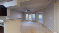 This single-floor residence offers a thoughtfully designed open-concept layout that seamlessly connects the living, dining, and kitchen areas. The living room is generously proportioned, featuring plush neutral carpeting, crown molding, a ceiling fan, and French doors that invite natural light and provide outdoor access. A decorative tray ceiling detail above the dining area adds architectural interest, complemented by an elegant pendant light fixture and a large mirror that amplifies the sense of space.

The kitchen is a standout feature, showcasing rich dark espresso cabinetry, granite countertops, a classic subway tile backsplash, and a full suite of stainless steel appliances. Wood-look flooring grounds the space, while a breakfast bar provides a casual dining option with direct sightlines into the living area.

The bedrooms are well-sized, each with soft carpeting, ceiling fans, and ample natural light from large windows dressed with blinds. The primary bedroom features a bay window configuration and an adjoining built-in desk or vanity area with additional shelving. Additional bedrooms are finished in the same neutral palette, offering versatile spaces.

The bathroom is finished with a granite-topped dark vanity, an undermount sink, a mirrored medicine cabinet, wood-look flooring, and a tiled soaking tub and shower combination, delivering a clean and cohesive aesthetic throughout.