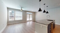 This well-appointed single-floor residence showcases a clean, modern design throughout. The open-concept living and kitchen area serves as the heart of the home, where light-toned hardwood-style flooring, neutral gray walls, and abundant natural light from large windows and French doors create a bright, welcoming atmosphere. A ceiling fan adds both function and style to the spacious living area, which opens directly to the outdoors via French doors fitted with transom windows above.

The kitchen is thoughtfully designed with crisp white cabinetry extending to the ceiling, a classic white subway tile backsplash, and striking granite countertops. A generously sized island with an undermount sink serves as a central workspace and casual gathering spot, illuminated by a trio of bold black industrial-style pendant lights. Stainless steel appliances, including a French door refrigerator with ice maker, a built-in microwave, and a range, complete the kitchen.

The bedroom features plush carpeting and access to a well-organized walk-in closet with built-in shelving and hanging rods. The bathroom offers a tiled tub and shower combination, a white vanity with granite countertop, and neutral tile flooring, maintaining the cohesive, contemporary aesthetic found throughout the home.