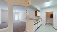 Located at 301 Converse Center St in Converse, Texas, Unit 711 is a single-story residence that offers a thoughtfully designed layout with warm, neutral tones throughout. The living area is generously sized, featuring soft carpet flooring, a ceiling fan, and a charming arched architectural detail that connects spaces with an elegant touch. A sliding glass door allows natural light to flow in and provides outdoor access. The front entry opens into a welcoming foyer with easy sightlines into the main living space.

The galley-style kitchen is efficiently arranged with ample white cabinetry accented by warm wood trim, light countertops, a double-basin sink, and white appliances including a range and refrigerator. Tile flooring runs through the kitchen, contrasting neatly with the carpet in adjacent areas. A peninsula counter connects the kitchen to the living area, enhancing the open feel of the home.

The bedrooms are comfortably proportioned, each with plush carpet, neutral walls, and windows fitted with blinds for natural light and privacy. Closet space is available within the bedrooms. The bathrooms feature tile flooring, wood-trimmed medicine cabinets, and clean white fixtures, with the primary bath offering a vanity with additional storage. Overall, the unit presents a clean, functional, and inviting living environment.