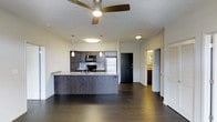 Located at 2131 N. Meridian, this single-floor residence showcases a thoughtfully designed open-concept layout that seamlessly connects the living and kitchen areas. Dark hardwood flooring runs throughout the main space, adding a rich, contemporary contrast to the light-colored walls and ceiling.

The kitchen is a standout feature, equipped with dark cabinetry, a stainless steel refrigerator, and black appliances including a range and microwave. A peninsula with a granite or stone-style countertop provides both additional workspace and a natural dividing point between the kitchen and living area. A sink is integrated into the peninsula, adding functionality to the layout. Pendant lighting hangs above the peninsula, complementing the ceiling fan with integrated lighting that illuminates the open living space.

A hallway leads from the main area to additional rooms, with a glimpse of what appears to be a bathroom with warm-toned cabinetry visible in the background. The overall ambiance is modern and understated, with clean lines, neutral tones, and practical finishes that create a cohesive and functional living environment.