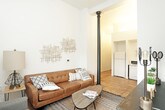 This two-floor residence offers a thoughtfully arranged layout across two distinct levels. The main floor features a welcoming living area with warm hardwood flooring, tall ceilings, and crisp white walls that create an open, airy atmosphere. A comfortable seating arrangement is complemented by decorative wall art, making the space ideal for relaxing or entertaining. The adjacent kitchen is efficiently designed in an L-shaped configuration, featuring dark cabinetry with brushed metal hardware, white countertops, open shelving, recessed lighting, and white appliances including a refrigerator, dishwasher, and microwave. Hardwood flooring continues throughout this level, adding warmth and continuity. A full bathroom on the upper level is finished with clean white surfaces, a combination tub and shower, a dark vanity with an integrated sink, and tile flooring. The upper level also hosts a carpeted bedroom with recessed lighting and clean white walls, offering a calm and restful environment. An additional bedroom features sloped ceilings and dual sliding-door closets, providing ample storage space. The overall design palette—neutral tones, modern fixtures, and a mix of hardwood and carpet—gives this multi-level space a clean, contemporary character suited for comfortable everyday living.