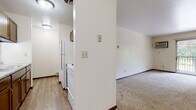This single-floor unit offers a functional and straightforward layout designed to maximize usable space throughout. The galley-style kitchen features warm wood cabinetry, a double-basin sink with light-toned countertops, and durable wood-look vinyl flooring. White appliances, including a refrigerator and range, are neatly positioned along one wall, while ample upper and lower cabinet storage lines the opposite side.

The living area is generously proportioned, finished with neutral wall-to-wall carpeting and crisp white walls. A sliding glass door opens to a private balcony overlooking mature trees, allowing natural light to fill the room. A baseboard heating unit runs along the exterior wall, providing consistent warmth throughout the space.

Two bedrooms are carpeted and well-sized, each with access to closet storage. One bedroom features a window with a pleasant outdoor view of surrounding greenery, complemented by a baseboard heater below.

The bathroom is neatly appointed, featuring a full tub-shower combination, a toilet, and a grey-toned vanity with a white countertop and wood-look vinyl flooring, offering a clean and updated aesthetic. Dark wood trim accents doors and baseboards throughout, providing a cohesive finish across the entire unit.