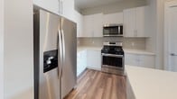 Located at 129 Parker St in Maynard, MA, this well-appointed single-floor residence offers a clean, modern aesthetic throughout. The open-concept living and kitchen area serves as the heart of the home, featuring rich hardwood-style flooring, recessed lighting, and a seamless flow between spaces. The kitchen is outfitted with stainless steel appliances — including a French door refrigerator with ice maker, gas range, and over-the-range microwave — complemented by crisp white cabinetry, neutral tile backsplash, quartz countertops, and a kitchen island with pendant lighting and wood-toned accents.

The bedrooms are finished with plush carpeting and are bathed in natural light through large windows with views of the surrounding neighborhood. Ceiling fans add comfort, and generous closet space is present throughout. The primary bathroom features a sleek glass-enclosed shower with white tile surround, a soaking tub, and access to a walk-in closet with built-in shelving. A second full bathroom includes a tub/shower combination, wood-look flooring, and a vanity with white countertops. The unit's neutral color palette and contemporary finishes create a clean, inviting atmosphere throughout.