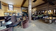 Located in Chicago's West Loop neighborhood, this single-floor space at 1515 W Monroe St masterfully blends historic industrial character with contemporary design. The interior is anchored by soaring ceiling heights, exposed brick walls, and dark structural beam detailing that give the space a commanding, loft-like atmosphere. Polished concrete floors reflect the abundant natural light that pours in through oversized, multi-pane windows stretching nearly floor to ceiling along the perimeter.

The layout is thoughtfully divided into distinct yet open zones. A welcoming lounge area features plush velvet seating in warm earth tones, bistro tables, and statement pendant lighting with Sputnik-style fixtures that add a modern contrast to the building's historic bones. A dedicated coffee bar is outfitted with professional equipment and shelving, serving as a natural social hub within the space.

Adjacent areas transition into darker, more intimate settings with leather seating, long communal tables, and bar-style counters backed by large mirrors. A private office or leasing area is equipped with a substantial dark desk and benefits from dramatic floor-to-ceiling windows. A striking steel staircase with an open railing adds vertical interest and connects to an upper mezzanine level. Lush potted plants are distributed throughout, softening the industrial aesthetic and adding vitality to the overall ambiance.