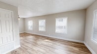 This two-story, 2-bedroom, 1-bathroom home is thoughtfully laid out with equal living space distributed across both floors. The main level features a bright, open combined living and dining area with light wood-style laminate flooring, neutral beige walls, white baseboards, and a textured ceiling. Multiple windows fitted with horizontal blinds allow natural light to pour in throughout. The kitchen is efficiently designed in a galley layout, offering warm medium-toned wood cabinetry, light granite-look countertops, a stainless steel double sink, and black appliances including a dishwasher. A window above the counter adds natural light to the workspace. The main floor also includes a staircase with white railings leading to the upper level. Upstairs, both bedrooms are carpeted in a neutral tan tone and feature textured walls, white trim, and windows with blinds. The spacious primary bedroom offers generous room and multiple closets are located throughout the home for ample storage. The full bathroom includes a tub-shower combination with white tile surround and a window for natural ventilation. With four closets total and a practical floor plan, this home balances comfort and functionality across both levels.