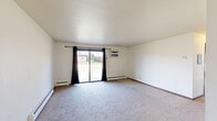 Located at 218 Royal Ct in Fox Crossing, Wisconsin, this single-floor residence offers three bedrooms and one bathroom within a practical and well-organized layout. The living area is carpeted and features a sliding glass door flanked by dark curtains, allowing natural light to fill the room while providing views of the surrounding outdoor greenery. A wall-mounted air conditioning unit and baseboard heating ensure year-round comfort. The open transition from the living space leads to a kitchen area equipped with built-in shelving and a ceiling fan overhead. The generously sized primary bedroom stands out as the largest room in the home, offering ample floor space, dual sets of bifold closet doors for abundant storage, and baseboard heating. Additional bedrooms are carpeted, each with windows that bring in natural light, closet space, and baseboard heaters. The full bathroom features warm-toned hardwood-style flooring, a single-sink vanity with white cabinetry, a tub-shower combination, and a ventilation fan. Throughout the home, white walls, wood-toned doors, and consistent trim details create a clean, cohesive aesthetic suited for comfortable everyday living.