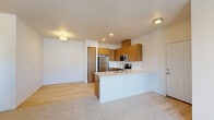 This single-floor residence offers a thoughtfully designed open-concept layout that seamlessly connects the kitchen and living areas. The kitchen is a standout feature, showcasing warm wood cabinetry paired with a crisp white quartz peninsula island that includes an undermount sink with a contemporary arc faucet. Stainless steel appliances—including a refrigerator, range, and microwave—are integrated throughout, complemented by recessed lighting and a clean white tile backsplash. Light hardwood-style flooring runs through the kitchen and transition areas, while plush neutral carpet adds comfort to the living and bedroom spaces.

The bedrooms are bright and simply appointed, with one featuring sliding glass door access to an exterior balcony and a wall-mounted HVAC unit. A ceiling fan is present in an additional bedroom, which also benefits from natural light. The bathroom is finished with a wood-toned vanity, white quartz countertop, large mirror, and a full tub-shower combination. A dedicated laundry room houses a side-by-side washer and dryer with built-in wire shelving above, adding practical convenience. The overall ambiance is clean, contemporary, and move-in ready.