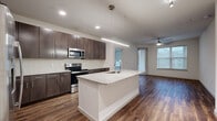 This 2-bedroom, 2-bathroom residence offers a well-organized and modern floor plan designed for comfortable everyday living. The open-concept kitchen and living area serves as the heart of the home, anchored by a large central island with a granite countertop and an integrated sink. Rich dark-espresso cabinetry extends to the ceiling, providing ample storage, while a full suite of stainless steel appliances—including a French door refrigerator, electric range, and over-the-range microwave—completes the kitchen. Wood-look plank flooring flows throughout the main living areas, adding warmth and visual continuity. The living room benefits from natural light and includes a ceiling fan. Both bedrooms feature plush carpeting, ceiling fans, and windows with roller shades that frame outdoor views. The primary bedroom connects to a dedicated closet with built-in shelving and hanging rods. One bedroom features wood-look flooring instead of carpet. Both bathrooms are finished with large-format gray tile flooring, dark wood vanities topped with granite countertops, framed mirrors, and soaking tubs with tile surrounds. Each bathroom also features a dedicated closet for additional storage, rounding out a highly functional and cohesive living space.