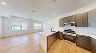 This well-appointed 2-bedroom, 2-bathroom residence at 100 Shepherds Ln in Totowa, NJ offers a thoughtfully designed single-floor layout with modern finishes throughout. The open-concept kitchen and living area serves as the heart of the home, featuring a large central island with a quartz countertop, an undermount sink, and a full suite of stainless steel appliances, including a gas range, microwave, and refrigerator. Warm-toned wood cabinetry and recessed lighting complete the kitchen's contemporary aesthetic, all set atop light hardwood flooring that flows seamlessly throughout the space. The generously sized primary bedroom features multiple windows that invite abundant natural light and offer views of the surrounding greenery, creating a bright and airy retreat. Both bedrooms are served by dedicated walk-in closets outfitted with built-in shelving systems and hardwood floors, providing ample and well-organized storage. The bathrooms are finished to a high standard, with one featuring a frameless sliding glass shower enclosure, large-format white wall tiles, and matte black fixtures for a sleek, modern look. A convenient hallway connects all rooms, contributing to the home's efficient and practical layout. Clean white walls, recessed lighting, and consistent hardwood flooring throughout unify the space with a cohesive, contemporary feel.
