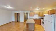 Located on Chapa Blvd in Elwood, Indiana, this single-floor home offers a functional and well-appointed layout designed for comfortable everyday living. The heart of the home is an open-concept kitchen and living area, where warm honey-toned oak cabinetry pairs with granite-look countertops and a central island that provides additional workspace and seating. White appliances, including a range, refrigerator, and double-basin sink, complete the kitchen. Recessed lighting and flush-mount fixtures illuminate the space, which flows seamlessly over durable light hardwood flooring throughout the main living areas. The spacious living room benefits from natural light through a large window, creating a bright and welcoming atmosphere. The bedrooms are carpeted for comfort and each feature windows that bring in natural light, with one room including a walk-in closet and direct access door. The home includes two bathrooms: one featuring a clean, all-white walk-in shower with a built-in bench seat, and another with a full soaking tub and shower combination. Consistent neutral wall tones, wood-trimmed doorways, and a practical, open floor plan give this home a cohesive and move-in-ready appeal.