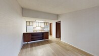 Located at 27010 Wentworth Dr in Roseville, Michigan, this one-bedroom, one-bathroom unit offers a practical and well-organized layout across a single floor. The open-concept living and kitchen area is anchored by light hardwood-style flooring and a textured ceiling, creating a bright and clean atmosphere. The kitchen is equipped with white appliances, including a refrigerator and electric range, and features warm wood-trimmed cabinetry with cream-colored doors, granite-style laminate countertops, and a skylight-style overhead light fixture that fills the space with additional brightness. A peninsula with a dark wood base and matching countertop extends into the living area, providing a convenient breakfast bar that visually connects the kitchen and living space. The bedroom is carpeted and comfortably sized, offering a ceiling fan with a light fixture, a window that allows natural light, and a full-size closet with wood-paneled bifold doors. Two closets provide ample storage throughout the unit. The bathroom features a full tub-shower combination with chrome fixtures and textured wall paneling. A hallway connects the main living areas to the bedroom and bathroom, and a utility room adds functional storage or laundry space. Overall, the unit presents a tidy, functional living environment in a compact and efficient footprint.