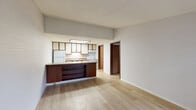 Located at 27010 Wentworth Dr in Roseville, Michigan, this one-bedroom, one-bathroom unit offers a practical and well-organized layout across a single floor. The open-concept living and kitchen area is anchored by light hardwood-style flooring and a textured ceiling, creating a bright and clean atmosphere. The kitchen is equipped with white appliances, including a refrigerator and electric range, and features warm wood-trimmed cabinetry with cream-colored doors, granite-style laminate countertops, and a skylight-style overhead light fixture that fills the space with additional brightness. A peninsula with a dark wood base and matching countertop extends into the living area, providing a convenient breakfast bar that visually connects the kitchen and living space. The bedroom is carpeted and comfortably sized, offering a ceiling fan with a light fixture, a window that allows natural light, and a full-size closet with wood-paneled bifold doors. Two closets provide ample storage throughout the unit. The bathroom features a full tub-shower combination with chrome fixtures and textured wall paneling. A hallway connects the main living areas to the bedroom and bathroom, and a utility room adds functional storage or laundry space. Overall, the unit presents a tidy, functional living environment in a compact and efficient footprint.