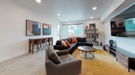 Located at 3269 Haven St in Oakland, CA, this single-floor space showcases a cohesive modern design with light wood-style flooring and recessed lighting throughout. The open-concept layout connects the kitchen, living, and dining areas, creating a fluid and functional flow.

The kitchen is outfitted with high-gloss dark gray cabinetry extending to the ceiling, providing generous storage. Stainless steel appliances—including a French door refrigerator, gas range, dishwasher, and microwave—complement the neutral countertops. A compact bar-height counter with wooden stools serves as a casual dining or workspace nook adjacent to the kitchen.

The living area is generously proportioned, featuring large windows that invite natural light and offer views of the surrounding neighborhood. A wall-mounted flat-screen TV, open shelving unit, and ample seating create a comfortable, well-appointed gathering space. A long wooden bar table with chairs provides an additional casual seating zone.

The dining room is a standout feature, distinguished by floor-to-ceiling navy and gold geometric wallcovering that lends a dramatic, intimate atmosphere. A sculptural pendant light fixture and dark furnishings complete the sophisticated aesthetic of this striking room.
