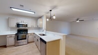 This single-floor residence offers a clean, functional layout designed for comfortable everyday living. The open-concept kitchen seamlessly connects to the living area, creating a bright and cohesive space. The kitchen is equipped with stainless steel appliances — including an electric range, over-the-range microwave, dishwasher, and refrigerator — paired with taupe cabinetry, white countertops, a peninsula with a single-basin sink, and a stylish multi-bulb pendant light fixture. Light wood-style flooring runs through the kitchen and entry areas, while a patterned tile backsplash adds a decorative touch.

The living area is generously sized with neutral carpet, white walls, a ceiling fan with light, and a front entry door flanked by a window with blinds that allows natural light to filter in.

Two bedrooms feature plush carpet, ceiling fans, natural light from windows with blinds, and sliding closets with built-in rods for ample storage. The two full bathrooms are finished consistently with warm wood-look flooring, taupe vanity cabinets with white countertops, and tiled shower-tub combos accented by a distinctive black tile border detail, giving each bathroom a classic yet polished appearance.