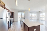 Located at S 34th St & Broadway in Council Bluffs, Iowa, this well-appointed 2-bedroom residence offers a thoughtfully designed single-floor layout. The open-concept living area seamlessly integrates the kitchen, dining, and living spaces, creating a bright and versatile environment. Large windows throughout flood the interior with natural light and frame sweeping views of the surrounding cityscape and skyline.

The kitchen is a standout feature, showcasing rich dark-walnut cabinetry that reaches toward the ceiling, a classic white subway tile backsplash, and a full suite of stainless steel appliances including a refrigerator, range, and built-in microwave. A generously sized center island with a white countertop and integrated sink serves as both a functional workspace and a casual gathering spot, complemented by stylish pendant lighting overhead.

The spacious primary bedroom includes plush carpeting, a ceiling fan, and sliding glass doors opening to a private balcony with outdoor views. The second bedroom features light hardwood-style flooring, large windows, and a ceiling fan. Bathrooms are finished with wood-tone vanities and clean white countertops. Additional highlights include multiple closets, an in-unit laundry area, and light hardwood-style flooring throughout the main living areas.