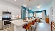 This stylish 2-bedroom, 2-bathroom residence is spread across a single floor and features a cohesive modern design anchored by striking teal accent walls, light wood-look flooring, and an abundance of natural light. The open-concept kitchen and living area serves as the heart of the home, where a spacious island with quartz countertops and seating for multiple bar stools flows seamlessly into the dining and living spaces. The kitchen is equipped with stainless steel appliances, white upper cabinetry, two-tone lower cabinetry, a subway tile backsplash, and elegant pendant lighting with brass accents. The living room is bright and inviting, featuring large windows with outdoor views, a ceiling fan, and a bold teal feature wall. Both bedrooms are well-sized, filled with natural light from large windows, and finished with the same warm wood-look flooring. The primary bedroom offers generous proportions and a dedicated closet. The bathrooms are finished with large-format tile flooring, soaking tub and shower combinations, and modern wood-toned vanities with clean countertops. A dedicated laundry room with a full-size washer and dryer and built-in shelving adds everyday convenience to this thoughtfully laid-out residence.