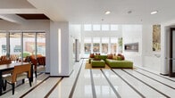 This contemporary single-floor space is defined by its striking architectural design and open, airy layout. Gleaming white tile floors with dark inlaid stripe accents run throughout, creating a bold, cohesive visual foundation across all areas.

The main lounge area features soaring double-height ceilings lined with expansive floor-to-ceiling windows and clerestory glazing, flooding the space with natural light and providing views of an outdoor pool and landscaping. A modern sectional sofa in earthy green anchors the space alongside a sleek wall-mounted fireplace. A separate seating nook near the entry showcases a stainless steel elevator, a marble-topped console, and vibrant artwork.

Multiple dining configurations accommodate both casual and social gatherings, including a high-top bar table with wicker stools and several standard dining tables with rattan-style chairs. A coffered ceiling with rich dark wood insets distinguishes the dining area, adding warmth and depth.

The fully equipped kitchen features dark espresso cabinetry, veined granite countertops, a professional-grade stainless steel range with a commercial hood, and full-size stainless appliances. Large glass sliding doors connect the dining area to an outdoor patio, enhancing the sense of openness throughout.