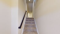 This three-story home is designed to maximize functionality across multiple levels, beginning with a ground-floor garage finished with a concrete floor and an automatic opener, offering generous vehicle and storage space. Carpeted stairs with a dark handrail and recessed lighting connect the floors, creating a clean, well-lit transition between levels.

The main living area features plush neutral carpeting, crown molding, and a white fireplace mantle that serves as a focal point. An open sightline connects the living space to an adjacent area with natural light filtering through blinds. The kitchen includes wood-look flooring, a stainless refrigerator, and a six-panel bifold closet door for pantry storage.

Bedrooms are carpeted and finished with neutral walls, textured ceilings, and natural light from windows with blinds. Crown molding is present in select rooms. A walk-in closet with wire shelving and a window adds practicality to one bedroom. The bathroom features a full tub-shower combo with brushed nickel fixtures and a clean white surround, maintaining the home's consistent, understated aesthetic throughout.