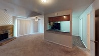 This two-story home offers a functional and comfortable layout across both levels. The living room serves as the heart of the space, showcasing vaulted ceilings, a ceiling fan, and a striking brick fireplace with a raised hearth and chevron-patterned wood surround above the mantle. Neutral carpet flooring and a sliding glass door with vertical blinds add to the room's welcoming atmosphere. An open pass-through window connects the living area to the kitchen, promoting a sense of flow between spaces. The kitchen is well-equipped with warm oak cabinetry, dark granite-look countertops, hardwood-style flooring, and black appliances including a range, over-the-range microwave, and refrigerator. The bedrooms are carpeted and finished with neutral tones, ceiling fans, and ample wall space, providing restful retreats. One bedroom offers direct access to an en suite bathroom. The bathroom features hardwood-style flooring, a dark-toned vanity with granite-look countertops, and a tiled tub and shower combo. Throughout the home, textured ceilings and consistent neutral color palettes create a cohesive, understated aesthetic that is both practical and move-in ready.