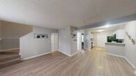 This two-story residence accommodates six bedrooms and three bathrooms distributed equally across both floors, connected by a central staircase. The main floor opens into a spacious living area finished with light-toned laminate wood flooring and neutral gray walls, creating a bright and cohesive atmosphere throughout. A textured ceiling adds subtle architectural character to the shared spaces.

The kitchen is a standout feature, designed in a galley-style layout with white cabinetry, white countertops, a gray tile backsplash, and black appliances including a range, dishwasher, microwave, and refrigerator. A peninsula counter separates the kitchen from the living area, enhancing the open flow between spaces.

The bedrooms are carpeted in a warm neutral tone and feature soft gray walls, each equipped with louvered bi-fold closet doors providing organized storage. The primary bedroom, while compact, is efficiently laid out.

The three bathrooms feature white vanities with ample counter space, large mirrors, and tub-shower combinations with tile surrounds. Overall, the residence offers a clean, practical design suited for multi-occupant living.