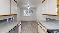 Located in Salem, Oregon, this two-bedroom, one-bathroom apartment offers a well-organized single-floor layout designed for comfortable, everyday living. The galley-style kitchen is a functional highlight, featuring white cabinetry with wood-tone trim, gray laminate countertops, light wood-look vinyl flooring, and a full suite of appliances including an electric range, refrigerator, and dishwasher. A dedicated in-unit laundry area is conveniently situated just off the kitchen. The kitchen flows into a dining area brightened by a window with outdoor views and a ceiling fan overhead. Both bedrooms are carpeted and finished with clean white walls, offering a calm and neutral atmosphere. The primary bedroom includes a wall-mounted thermostat and built-in closet storage, while the second bedroom features a wide sliding double-door closet and natural light from a large window overlooking the surrounding greenery. The shared bathroom is finished with wood-look vinyl flooring, a single-sink vanity with a speckled countertop, and a full tub-shower combination. Throughout the unit, the light color palette and consistent finishes create a bright, cohesive feel suited for practical, comfortable living.