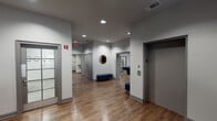 This well-appointed single-floor amenity facility offers a variety of thoughtfully designed spaces connected by wide, light-filled corridors. The hallways feature warm wood-look flooring, neutral gray walls, recessed lighting, and frosted glass doors, creating a clean and welcoming flow throughout the space.

The fitness and yoga studio is a standout area, boasting a tray ceiling with a ceiling fan, floor-to-ceiling mirrors along one wall, vibrant striped accent walls in red, orange, teal, and blue, and large windows that invite abundant natural light and panoramic outdoor views. The open, polished hardwood floor makes it ideal for group exercise and movement activities.

Adjacent to the studio is an observation or support area with oversized interior windows overlooking the fitness space, along with a built-in counter — well-suited for instructors or administrative use.

The lounge and media room features a dramatic dark accent wall with an orange-trimmed built-in entertainment center, a large flat-screen television, and ample cabinetry. Comfortable gray armchairs, a teal ottoman, and a wood coffee table complete the cozy, modern aesthetic.

A dedicated games room houses a full-size pool table and connects seamlessly to the main corridor. Throughout the space, decorative touches such as a round wall mirror, woven wall art, and framed prints add character and warmth to the overall environment.