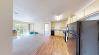 Located at 14002 Linden Ave N in Seattle, WA, this single-floor unit offers four bedrooms and one bathroom within a compact, efficiently designed floor plan. The open-concept living and kitchen area serves as the heart of the home, featuring warm hardwood-style flooring that extends through the main space. The kitchen is equipped with light maple cabinetry, a gas range, dishwasher, and a full-size refrigerator, all in black finishes that contrast neatly with the light cabinetry and neutral countertops. A skylight above the kitchen area adds a touch of natural brightness. The living area opens to a balcony through sliding glass doors, allowing natural light to pour in and providing a pleasant outdoor view of surrounding greenery. Each of the four bedrooms is carpeted and features built-in closets with sliding or bifold doors. Several bedrooms benefit from windows with blinds, offering natural light and neighborhood views. Baseboard heating is present in the bedrooms for year-round comfort. The single bathroom is finished with hardwood-style flooring, a vanity with ample cabinetry, and accessibility-friendly grab bars. The overall aesthetic is clean, neutral, and functional, making this unit a practical choice in the Broadview neighborhood of Seattle.