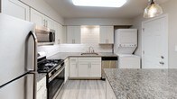 This single-story, two-bedroom, one-bathroom residence offers a thoughtfully designed layout with modern finishes throughout. The kitchen serves as a functional centerpiece, featuring white shaker cabinetry, granite countertops, a classic white subway tile backsplash, and a full suite of stainless steel appliances including a gas range, microwave, and dishwasher. An undermount stainless steel sink with a brushed nickel faucet adds a refined touch. A stacked washer and dryer unit is conveniently integrated within the kitchen area, streamlining daily routines.

The two bedrooms share a consistent aesthetic, each showcasing durable wood-look flooring, neutral gray walls, and ceiling fans with integrated lighting. Windows in each bedroom bring in natural light and offer views of surrounding greenery. Closet space is provided in at least one bedroom, featuring a standard rod-and-shelf configuration.

The full bathroom is clean and efficient, outfitted with a tub-shower combination, brushed nickel fixtures, a toilet, an overhead storage cabinet in white, and a vanity with a marble-style countertop. The overall ambiance of the unit is bright, neutral, and move-in ready.