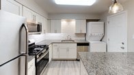 This single-story, two-bedroom, one-bathroom residence offers a thoughtfully designed layout with modern finishes throughout. The kitchen serves as a functional centerpiece, featuring white shaker cabinetry, granite countertops, a classic white subway tile backsplash, and a full suite of stainless steel appliances including a gas range, microwave, and dishwasher. An undermount stainless steel sink with a brushed nickel faucet adds a refined touch. A stacked washer and dryer unit is conveniently integrated within the kitchen area, streamlining daily routines.

The two bedrooms share a consistent aesthetic, each showcasing durable wood-look flooring, neutral gray walls, and ceiling fans with integrated lighting. Windows in each bedroom bring in natural light and offer views of surrounding greenery. Closet space is provided in at least one bedroom, featuring a standard rod-and-shelf configuration.

The full bathroom is clean and efficient, outfitted with a tub-shower combination, brushed nickel fixtures, a toilet, an overhead storage cabinet in white, and a vanity with a marble-style countertop. The overall ambiance of the unit is bright, neutral, and move-in ready.