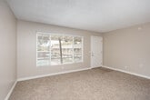 Located at 1921 W La Veta Ave in Orange, California, this one-bedroom, one-bathroom residence offers a practical and comfortable single-floor layout. The living room is carpeted in a neutral tone, featuring a textured ceiling and a wall-mounted HVAC vent, with a large sliding glass door that fills the space with natural light and provides views of the surrounding exterior. The open layout connects the living area to the combined dining and kitchen space, where light hardwood-style flooring, crisp white cabinetry, white countertops, and a gas range create a clean, functional kitchen. A window above the sink brings in additional natural light. The bedroom is generously sized, featuring soft carpeting, a ceiling fan with integrated lighting, and a built-in closet with a hanging rod for organized storage. The unit benefits from four closets in total, offering substantial storage throughout. The bathroom includes a white vanity with a mirror cabinet above, a towel ring, and access to an adjacent hallway. Neutral beige tones carry throughout the residence, creating a cohesive and understated aesthetic. The single-floor plan ensures ease of movement between all areas, making this a well-organized and efficient living space in the heart of Orange, CA.