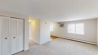 Located at 18 N Oak Ave in Clifton Heights, Pennsylvania, this single-floor unit offers a clean, functional layout designed for comfortable everyday living. The open living area is finished with neutral-toned carpeting and bright white walls, creating a light and airy atmosphere. Natural light filters in through multiple windows fitted with blinds, while a wall-mounted air conditioning unit and baseboard heating ensure year-round comfort. A louvered bifold closet provides convenient storage directly off the living space. The kitchen features white shaker-style cabinetry extending to the ceiling for generous storage, complemented by a marble-style backsplash, gray laminate countertops, a stainless steel sink, and white appliances including a coil-top range and refrigerator. Warm hardwood flooring grounds the kitchen area. The bedroom is generously proportioned with soft carpeting, a large window overlooking the outdoors, and an impressive wall of dual bifold closets offering abundant storage. The bathroom is finished with warm golden tile flooring and tiled shower walls in earthy tones, paired with a white vanity and sink. The overall design is clean and understated, offering a move-in-ready space with practical amenities throughout.