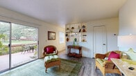 Located at 7212 Carlton Arms Dr in New Port Richey, Florida, this single-floor residence offers a well-organized layout with a warm, welcoming ambiance throughout. The living room is a comfortable and inviting space, featuring wood-look flooring, a teal area rug, and a large sliding glass door that fills the room with natural light and provides direct access to a private outdoor patio overlooking lush greenery. A decorative slatted shelving unit serves as a charming divider between the living and dining areas, adding architectural character to the open flow. The dining area is well-defined and accented by an elegant chandelier overhead, hardwood-style flooring, and a bright window that brings in additional natural light. The kitchen is equipped with warm oak cabinetry, laminate countertops, a stainless steel sink, and a full range with overhead ventilation. The bedroom offers a cozy retreat with plush carpeting, ample natural light through a window with blinds, and a generous double-door closet for storage. The bathroom features a full tub-shower combination, a wide vanity with an integrated sink, and a window for ventilation and light. Throughout the home, neutral wall tones and consistent flooring create a cohesive and functional living environment.
