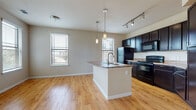 This single-floor unit is designed with an open-concept layout that seamlessly connects the kitchen and living area, creating a bright and functional living space. Warm honey-toned hardwood-style flooring extends throughout, providing a cohesive and inviting atmosphere across all rooms.

The kitchen is a standout feature, equipped with dark espresso cabinetry that extends to the ceiling for ample storage, granite-style countertops, and black stainless appliances including a refrigerator, electric range, and built-in microwave. A central island with a built-in sink and pendant lighting above serves as both a prep area and casual gathering point. Track lighting adds additional illumination to the kitchen zone.

The living area benefits from multiple windows fitted with blinds, allowing abundant natural light while maintaining privacy. A glazed exterior door provides direct outdoor access and further brightens the space.

The bedrooms feature ceiling fans, generous closet space with built-in shelving, and continued hardwood-style flooring. Two bathrooms are finished with dark vanity cabinetry, granite-style countertops, and large mirrors. The primary bathroom includes a tiled tub-shower combination, while the secondary bathroom offers a clean, efficient layout. Neutral wall tones throughout create a calm, versatile backdrop.