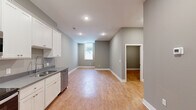 This single-floor, 2-bedroom, 1-bathroom residence offers a clean, modern aesthetic throughout. The open-concept kitchen and living area serves as the heart of the home, featuring warm wood-look flooring, recessed lighting, and neutral gray walls that create a bright, cohesive atmosphere. The kitchen is well-equipped with white shaker-style cabinetry, gray countertops, and a full suite of stainless steel appliances including a refrigerator, electric range, over-the-range microwave, and dishwasher. A window at the far end of the living area brings in natural light, enhancing the sense of openness. Both bedrooms continue the consistent flooring and neutral color palette, with each room offering a generously sized double-door closet fitted with built-in shelving and hanging rods for organized storage. The primary bedroom provides a comfortable footprint suitable for a full bedroom setup. The shared bathroom is finished to a high standard, featuring marble-look tile flooring, a white vanity with brushed nickel hardware, and a tub/shower combination with white subway tile surround accented by a decorative blue mosaic border tile. The overall design emphasizes clean lines and functional, move-in-ready living.