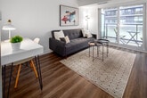Located at 20 Samuel Wood Way in Toronto's Etobicoke district, this thoughtfully designed single-floor unit offers a clean, modern aesthetic throughout. The entry corridor sets the tone with crisp white walls, wood-look flooring, and a slim console table with a round mirror — a functional yet stylish welcome.

The kitchen is outfitted with flat-front white cabinetry, white quartz countertops, a subway tile backsplash, a stainless steel undermount sink, a built-in cooktop, and an over-the-range stainless steel microwave — delivering a cohesive, contemporary look.

The open living area is bright and inviting, featuring large floor-to-ceiling sliding glass doors that lead to a private balcony, allowing natural light to fill the space. The living room comfortably accommodates a sofa, coffee table, and a dedicated workspace with a compact desk and chair, making it versatile for both relaxation and productivity.

The sleeping area enjoys direct balcony access through its own sliding glass door, further enhancing the sense of openness. Wood-look flooring flows consistently throughout the unit, tying each area together with a warm, unified finish. The overall ambiance is light, airy, and minimalist — ideal for modern urban living.