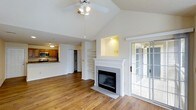 Located at 100 Crescent Arbor Ln in Cary, NC, this single-floor home offers a thoughtfully designed open-concept layout that blends comfort and functionality. The main living area immediately impresses with soaring vaulted ceilings and warm hardwood flooring that flows throughout the space. A classic white-mantled fireplace with tile surround serves as the focal point of the living room, flanked by built-in shelving that provides both storage and display space. A ceiling fan with integrated lighting enhances airflow and illumination in the living area. Natural light pours in through a set of French doors that lead directly to an outdoor patio or porch, creating a seamless indoor-outdoor connection. The open layout connects the living area directly to the kitchen, which features warm wood cabinetry, a breakfast bar peninsula, and stainless steel appliances — ideal for entertaining or casual dining. The neutral color palette throughout the home creates a bright, welcoming ambiance, while the architectural details such as the vaulted ceiling and built-in niches lend the space a distinctive character. The overall design balances practical living with stylish touches, making this Cary home both inviting and versatile.
