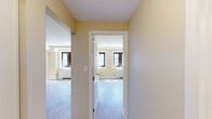 This thoughtfully designed 1-bedroom, 1-bathroom unit offers a functional and comfortable layout across a single floor. Light-toned hardwood-style flooring flows consistently throughout, creating a cohesive and clean aesthetic.

The galley-style kitchen is a standout feature, equipped with stainless steel appliances including a refrigerator, electric range, microwave, and dishwasher. White shaker cabinetry provides ample storage, while dark granite countertops add a striking contrast. Recessed lighting and a stainless steel sink complete the space.

The combined kitchen and living area transitions into a bright, open living room featuring warm beige walls, multiple windows with dark-framed casings, and a radiator heating unit. Built-in shelving along one wall offers convenient display and storage options.

The bedroom is a comfortable, well-proportioned room with warm neutral tones, hardwood-style flooring, and a sliding door closet for organized storage. Natural light enters through a window, contributing to the room's welcoming atmosphere.

A connecting hallway links the main living areas to the bedroom and bathroom with ease. The bathroom features a tiled tub-shower combination with beige stone-look tile surround, a toilet, and a white vanity.

Overall, the unit presents a clean, neutral palette with practical finishes suited for comfortable everyday living.