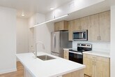This well-appointed 2-bedroom, 2-bathroom residence offers a thoughtfully designed single-floor layout with a clean, contemporary aesthetic throughout. The open-concept kitchen serves as the heart of the home, anchored by a large center island with a white quartz countertop, an undermount stainless steel sink, and a sleek linear pendant light overhead. Light wood cabinetry extends to the ceiling, paired with a full suite of stainless steel appliances including a refrigerator, electric range, and built-in microwave. Warm hardwood-style flooring flows through the main living areas, complementing the bright white walls and recessed lighting. The living area opens directly to a private balcony through sliding glass doors, filling the space with natural light. A ceiling fan adds a functional accent to both the main living area and each bedroom. The spacious primary bedroom features plush carpeting, wide windows with outdoor views, and ample room to furnish comfortably. The second bedroom mirrors this layout with its own window and ceiling fan. Both bathrooms are finished in a clean, modern style with hardwood-style flooring, white tub-shower combinations, and light wood vanities with white countertops. The overall ambiance is bright, airy, and move-in ready.