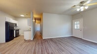 This single-story space is designed with a clean, functional layout that flows naturally from room to room. The interior is unified by durable wood-look flooring that runs consistently throughout, complementing the neutral gray and white color palette across all spaces.

The living area is open and well-proportioned, featuring a ceiling fan and a front entry door with a window that allows natural light to filter in. Adjacent to the living space, the kitchen is equipped with black appliances including a refrigerator, range, and microwave, set against crisp white cabinetry and granite-style countertops. A pendant chandelier adds a decorative touch above the neighboring dining area.

A central hallway connects the living spaces to the private areas of the unit. The bedrooms are comfortably sized, each with neutral walls, wood-look flooring, and ceiling fans or windows with blinds for light control. One bedroom features a built-in desk with granite-style countertop, adding functional workspace. A double-door closet provides ample storage.

Both bathrooms maintain a consistent design with white cabinetry, granite-style vanity tops, and tub-shower combinations. The overall ambiance is clean, modern, and move-in ready.